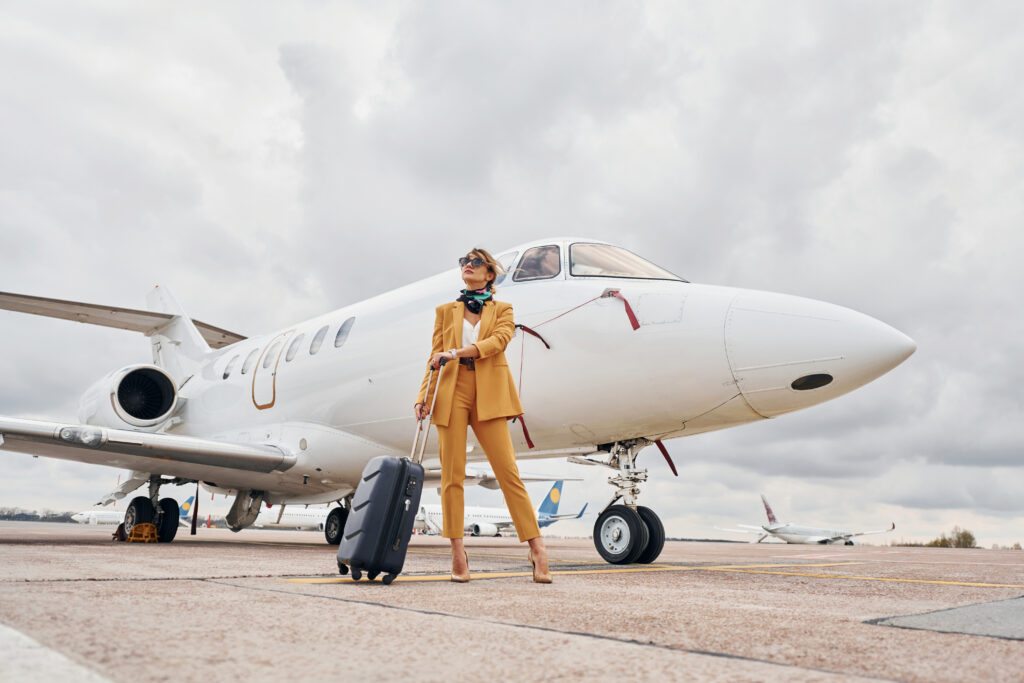 elegant clothes. young woman with luggage is outdoors near airplane